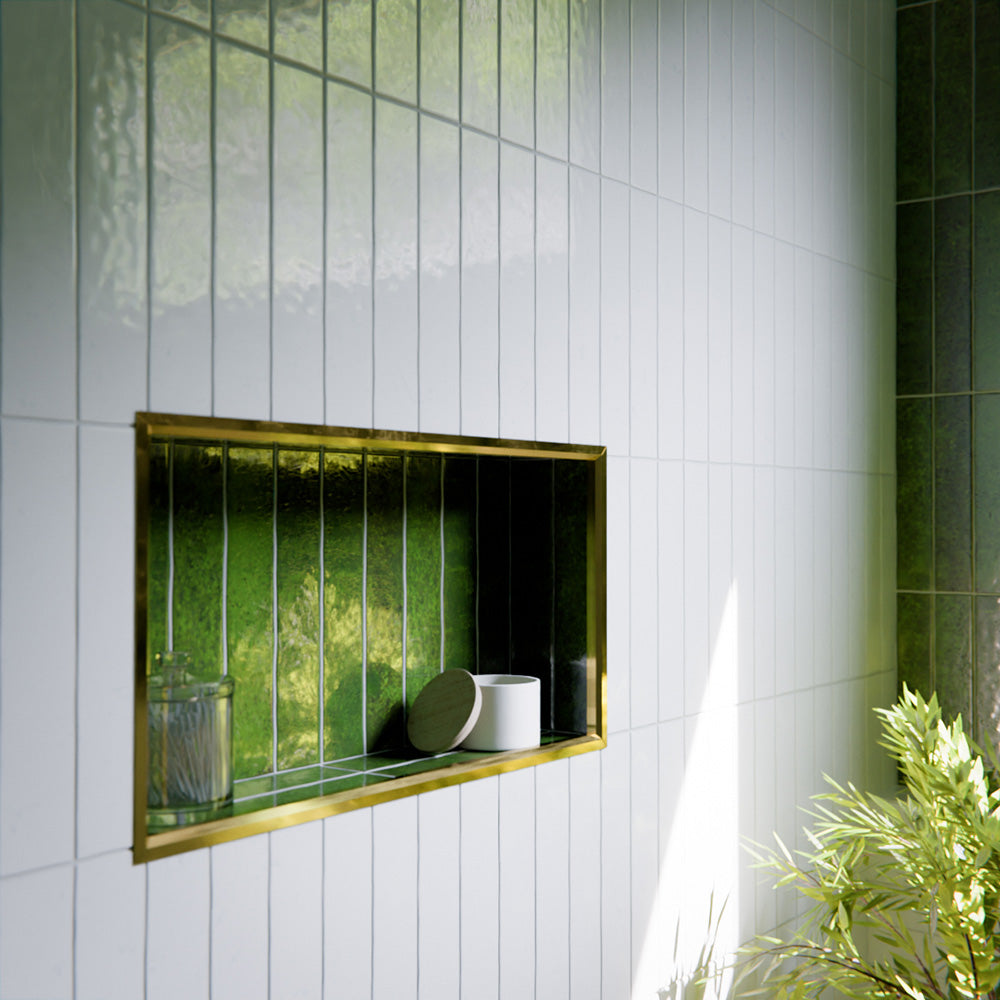 Modern bathroom featuring Bora Bora White Sand Brick ceramic wall tiles in a 6.5 × 32.8cm slim brick format with a flux glaze finish, laid vertically and horizontally to create a soft, textured feature wall, paired with a freestanding bath, brass tapware, natural light, and greenery for a calm, spa-like atmosphere.