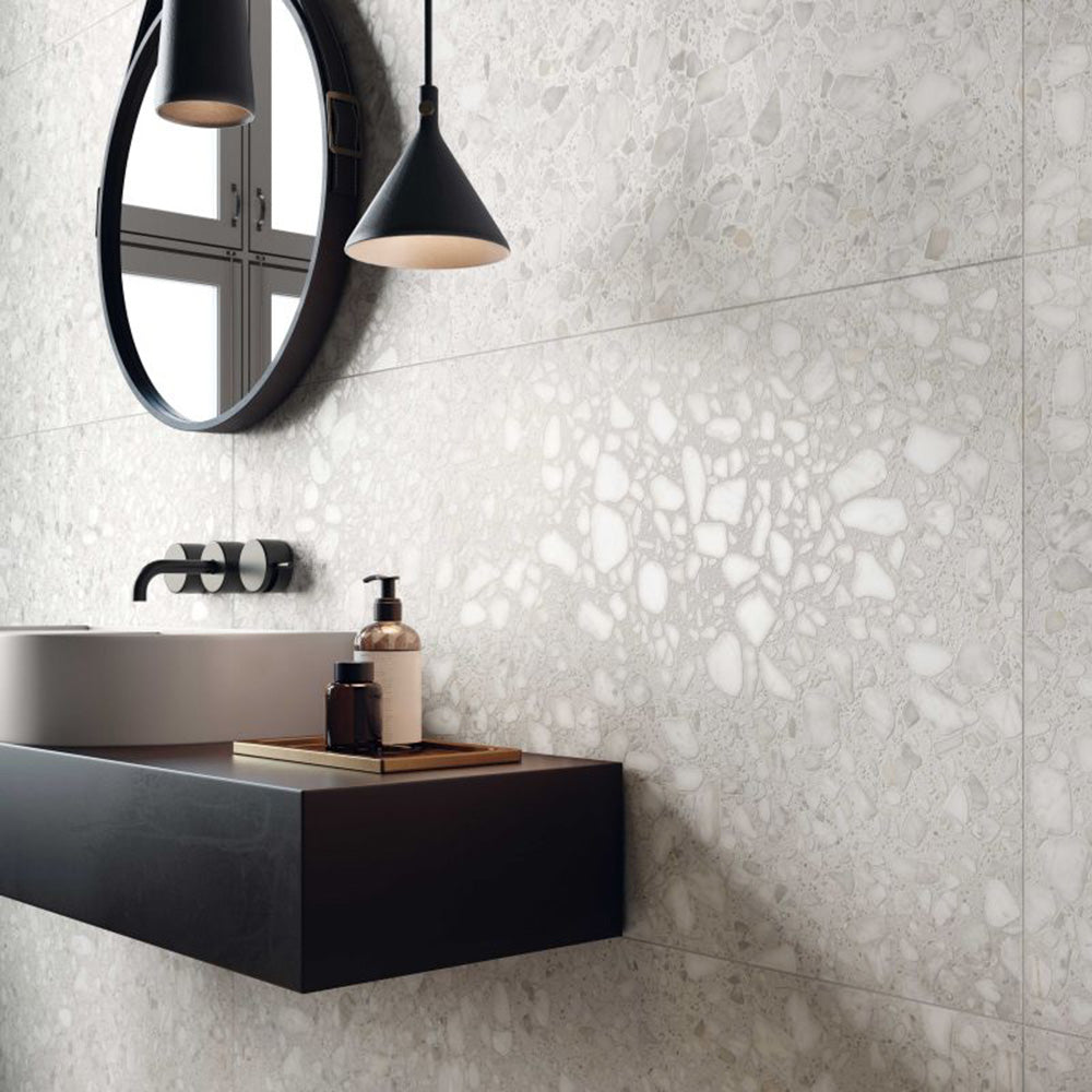 Contemporary bathroom featuring Shards Blanco 3D Terrazzo 60x120cm porcelain wall tiles, showcasing a white terrazzo effect with textured 3D stone chips, paired with a black floating vanity, matte black fittings, round mirror and modern pendant lighting.