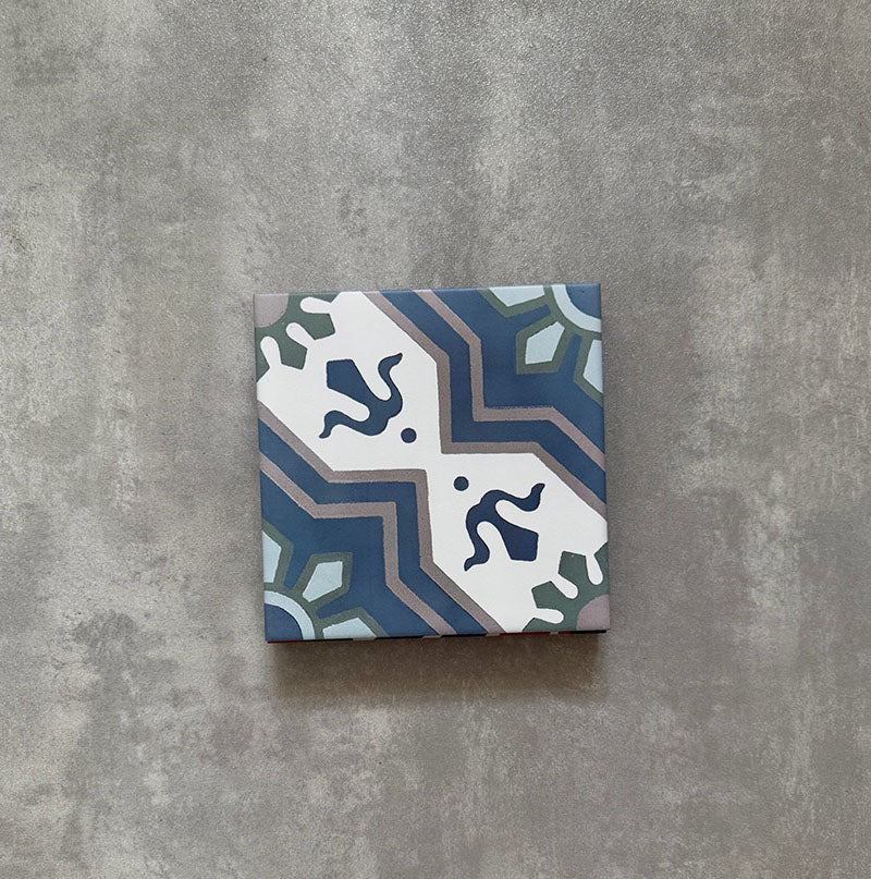 Single Balthazar Blue 20×20cm Moroccan-style porcelain tile displayed against a neutral stone-effect background, highlighting the intricate geometric pattern in layered blue, teal, soft grey and white tones with an encaustic-inspired matt finish.