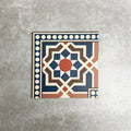 Single Balthazar Grand Corner 20×20cm porcelain tile displayed against a neutral stone-effect background, featuring a Moroccan-inspired geometric corner border design in deep blue, warm brown, terracotta and cream tones, designed to frame patterned layouts with a cohesive, decorative finish.