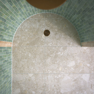 Walk-in shower featuring Essentials Terrazzo Stone Avorio 60x120cm terrazzo effect porcelain wall and floor tiles, paired with green glazed brick wall tiles, arched ceiling detail, and a brushed brass shower drain.