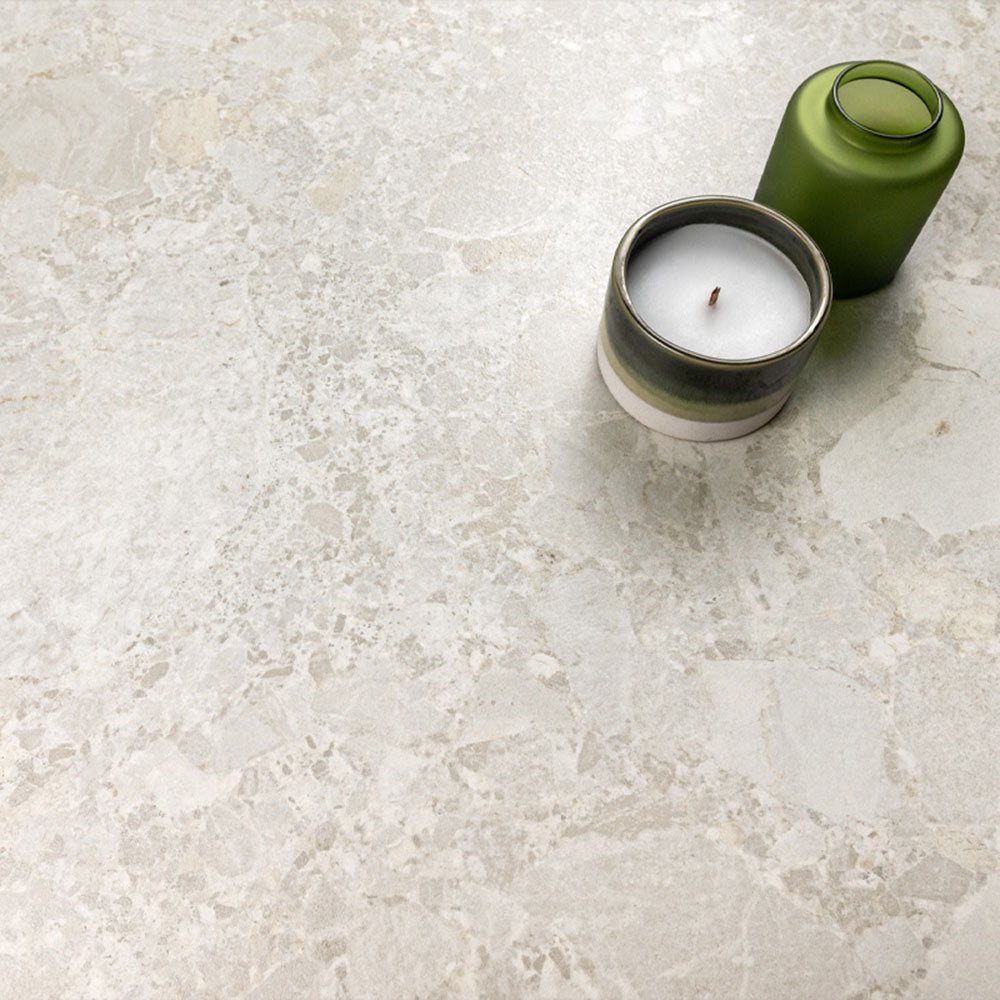 Kitchen surface featuring Essentials Terrazzo Stone Blanca 60x120cm terrazzo effect porcelain tiles, styled with a ceramic candle and green glass vessel, highlighting soft white and beige stone-inspired variation.