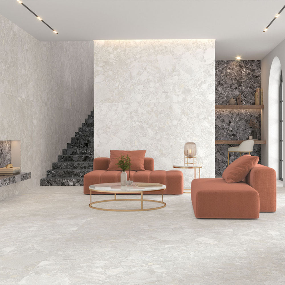 Living room interior featuring Essentials Terrazzo Stone Blanca 60x120cm terrazzo effect porcelain floor tiles, paired with matching wall surfaces, dark terrazzo feature shelving, and soft coral seating for a contemporary, design-led space.