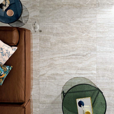 Living room featuring Taj Mahal Polished Marble effect 60 × 120cm porcelain floor tiles, styled with a leather sofa, glass side tables, and layered cushions, highlighting soft beige tones and natural flowing veining.