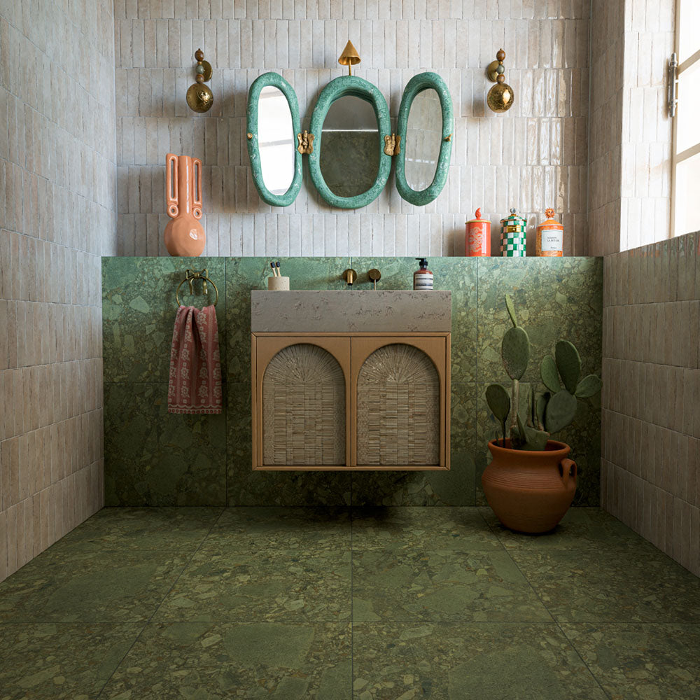 Bathroom featuring Terrazerri Terrazzo Green 60x60cm tiles, showcasing a rich green terrazzo effect surface with layered stone-inspired fragments and natural tonal variation. Used across the floor and lower walls, the large-format tiles create a seamless, luxurious look, while the soft neutral wall tiles, natural textures and decorative accents add warmth and contrast. The result is a bold yet elegant space inspired by Mediterranean design and contemporary interiors.