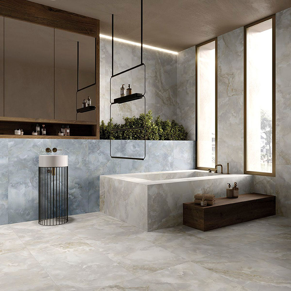 Contemporary luxury bathroom featuring Thebes Blue Honed Matt Onyx porcelain tiles on the walls and bath surround. The soft blue onyx-effect veining pairs beautifully with warm wood cabinetry, black accents and large-format stone effect floor tiles to create a calm, spa-inspired space.