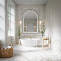 Elegant bathroom featuring Thebes White honed matt onyx effect porcelain wall and floor tiles in a 60cm x 60cm format, paired with a freestanding bath, classic wall panelling, an arched mirror, brushed brass fittings and soft neutral styling for a timeless luxury look.