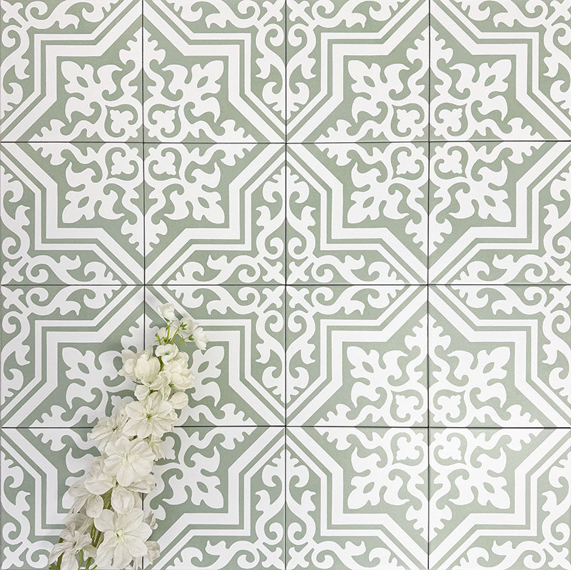 Flat lay of London Streets Thornton Place Sage Green 20cm x 20cm Victorian Moroccan style tiles arranged in a repeating pattern, featuring intricate white motifs on a sage green background with decorative white flowers.
