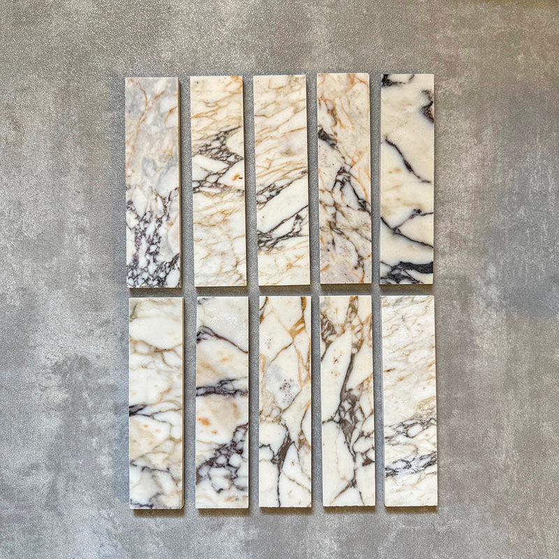 Set of Fayrouz Picasso 5x20cm natural marble tiles with a honed finish, displaying a white base with expressive grey, green and warm gold veining, showcasing natural tonal variation and unique patterning across individual pieces.