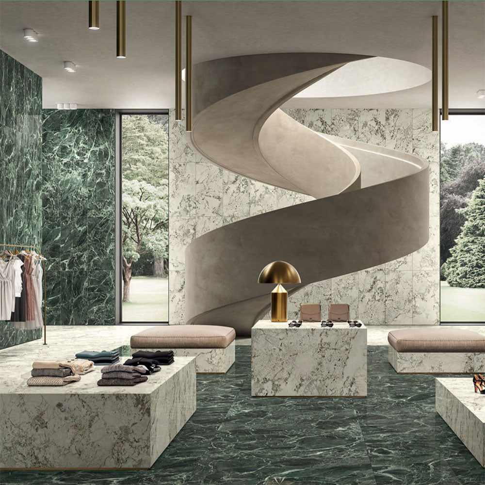 Retail interior featuring Verde Apia Polished Green Marble effect 60 × 60cm porcelain wall and floor tiles, styled with sculptural staircase, stone display plinths, and rich green tones with striking natural veining.
