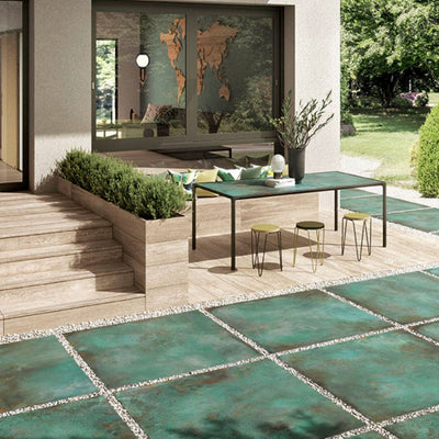 Outdoor patio featuring Verde Copper Oxide 2cm thick porcelain floor tiles in a metallic effect finish, styled with contemporary garden furniture, timber-effect steps, built-in planters and modern landscaping for a luxurious outdoor living space.