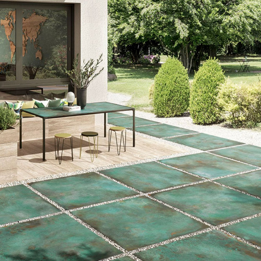 Outdoor patio featuring Verde Copper Oxide 2cm thick porcelain floor tiles in a metallic effect finish, styled with contemporary garden furniture, timber-effect steps, built-in planters and modern landscaping for a luxurious outdoor living space.