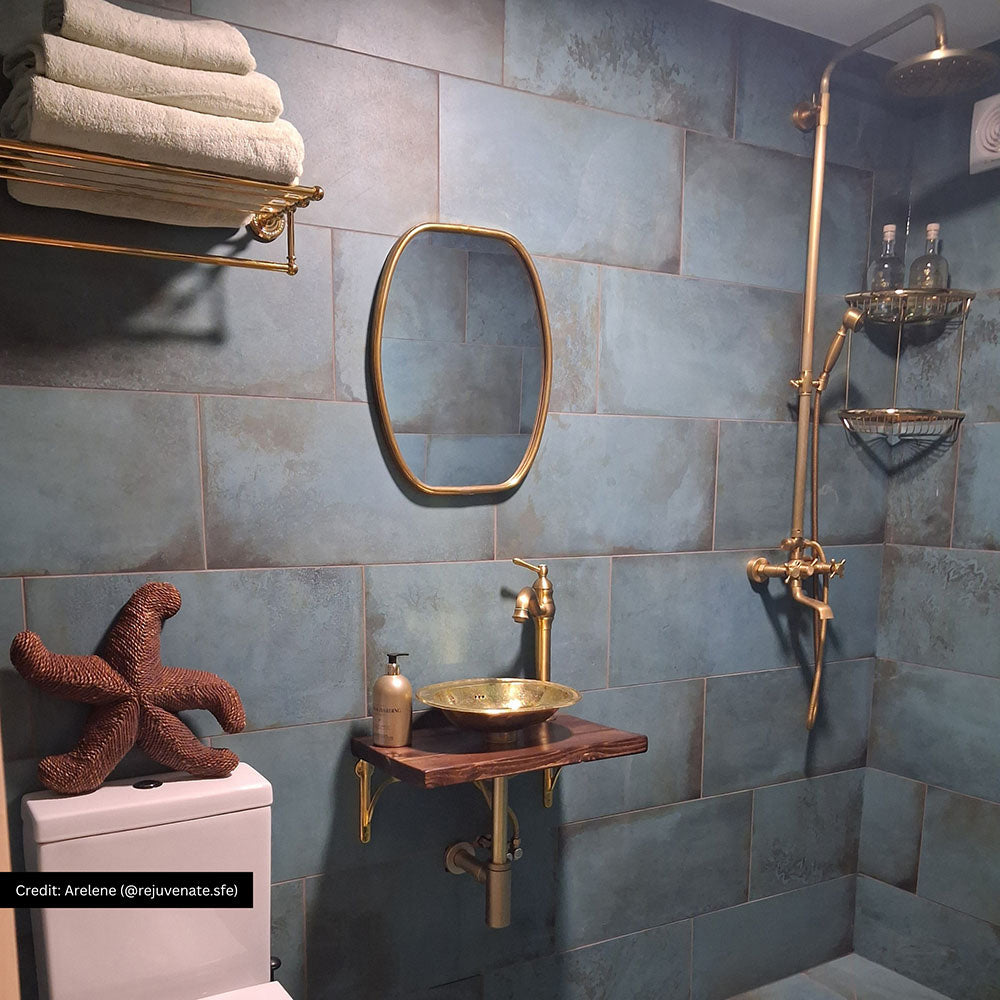 Bathroom featuring Verde Copper Oxide 30cm x 60cm metallic effect wall tiles, styled with brass shower fittings, a wall-mounted basin, wooden shelf and warm contemporary décor.