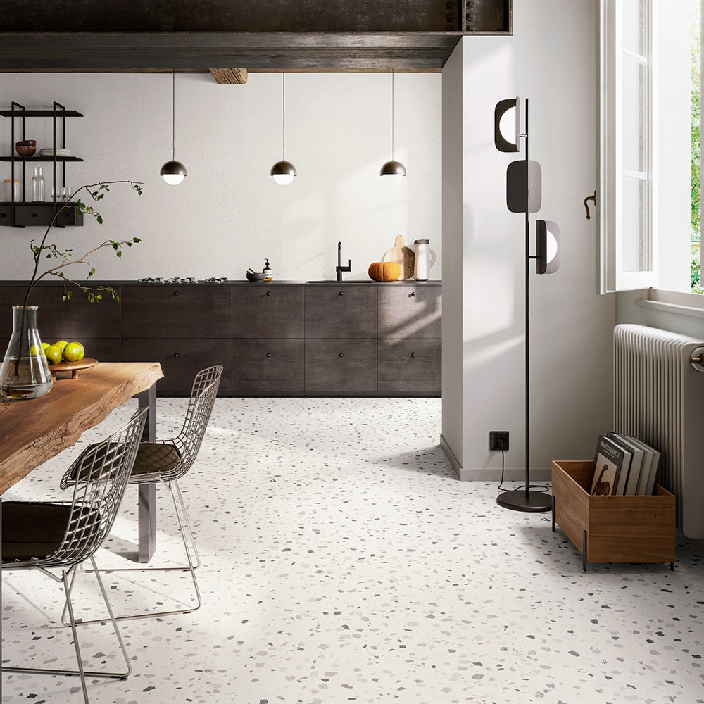 Open-plan kitchen and dining area featuring Verona Medium White concrete effect porcelain floor tiles with a terrazzo-inspired finish, complemented by dark wood cabinetry, black lighting, natural timber furniture and contemporary minimalist styling.