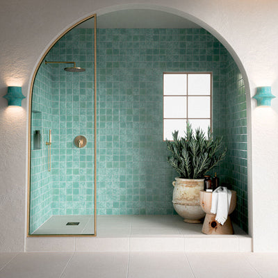 Contemporary walk-in shower featuring Verona Micro Sand 60cm x 60cm terrazzo effect porcelain wall tiles, paired with white floor tiles, brass shower fittings and an arched alcove for a Mediterranean-inspired bathroom.