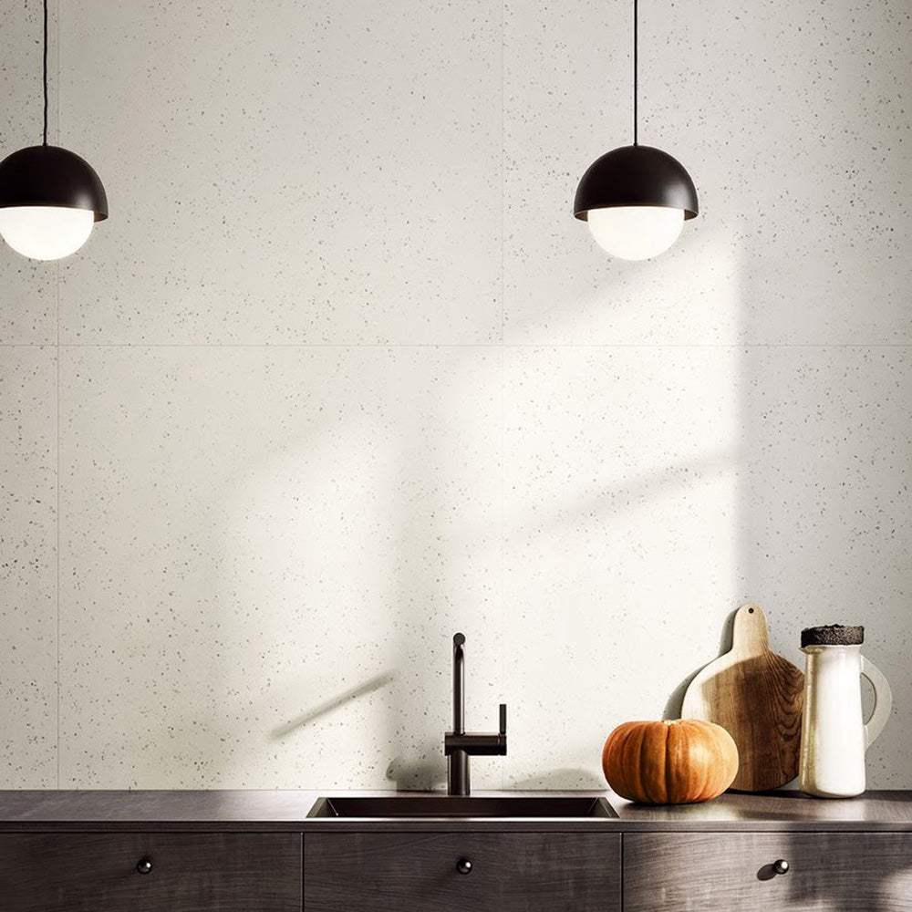 Contemporary kitchen featuring Verona Micro White concrete effect porcelain wall tiles, styled with dark cabinetry, black pendant lighting, warm wood accessories and minimalist décor for a bright, modern interior.