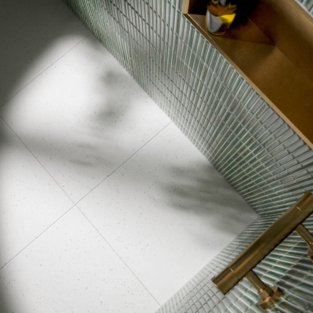 Bathroom interior featuring Verona Micro White 60 × 60cm terrazzo concrete-effect porcelain floor tiles, showcasing a soft white surface with delicate speckled detailing, paired with pale green mosaic wall tiles and warm brass fittings for a clean, contemporary finish.