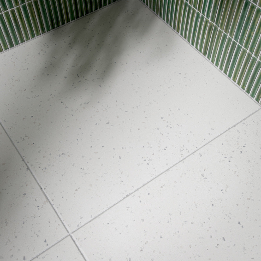 Bathroom interior featuring Verona Micro White 60 × 60cm terrazzo concrete-effect porcelain floor tiles, showcasing a soft white surface with delicate speckled detailing, paired with pale green mosaic wall tiles and warm brass fittings for a clean, contemporary finish.