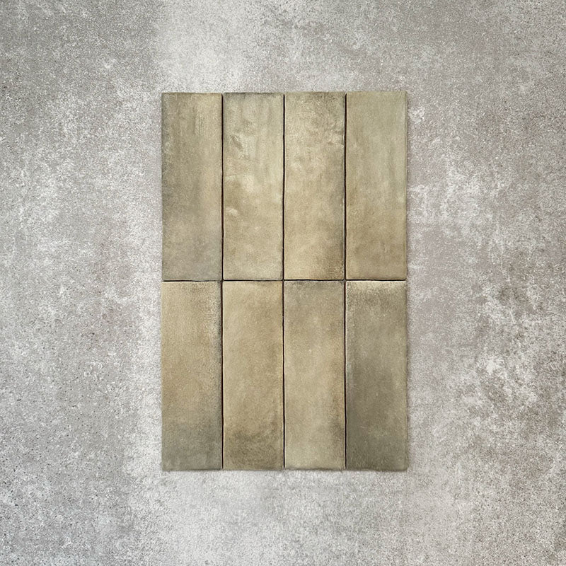 Flat lay of Zellige Weald Green 6.5×20cm Moroccan-style ceramic brick tiles, highlighting soft green and earthy tonal variation, irregular edges and a handmade-look glazed finish on a neutral background.