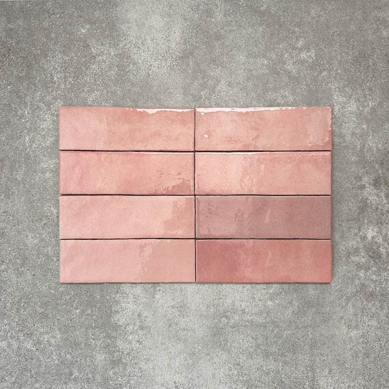 Flat lay of Zellige Rose Pink Brick 6.5 × 20cm Moroccan-style ceramic tiles, shown in soft blush, dusty rose and terracotta pink tones with gentle tonal variation and lightly uneven edges, arranged in a vertical brick layout on a textured grey background to showcase the handcrafted zellige-effect glaze.