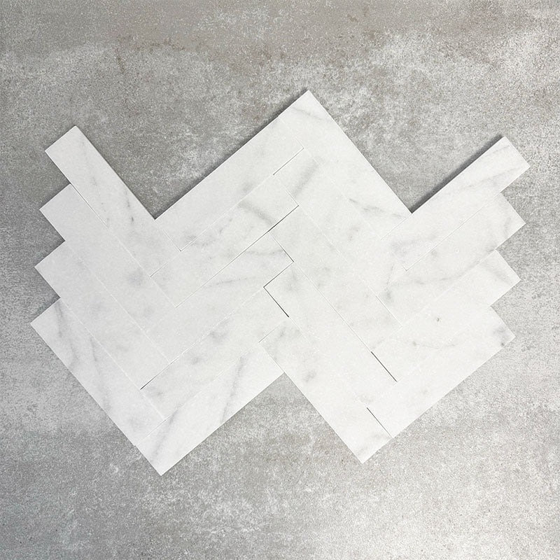 Arrangement featuring Fayrouz White 5x20cm natural marble tiles with a honed finish, laid in a herringbone pattern to create directional movement, showcasing a soft white base with subtle grey veining and gentle tonal variation.