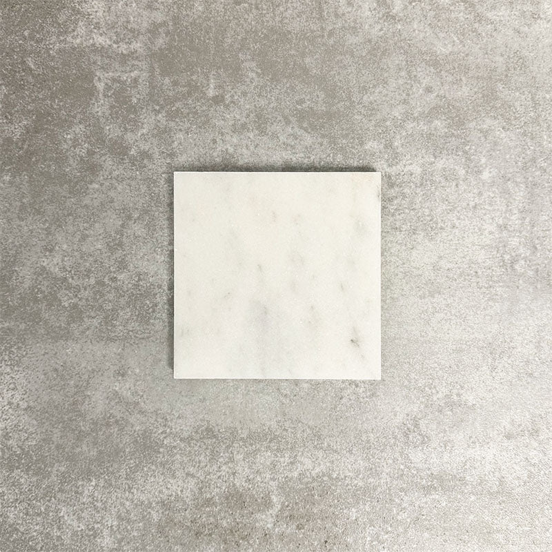 Single Fayrouz White 15.2x15.2cm natural marble tile with a honed finish, featuring soft white tones and subtle natural markings, displayed against a neutral textured background in a clean product setting.
