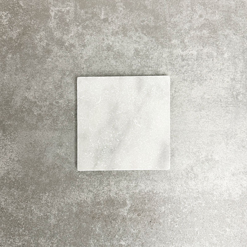 Single Fayrouz White 15.2x15.2cm natural marble tile with a tumbled finish, featuring soft white tones and subtle natural veining, displayed against a neutral textured background in a clean product setting.