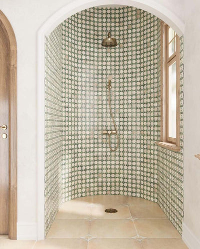 Walk-in shower featuring Zanzibar Moroccan Emerald Green ceramic wall tiles in a repeating Moroccan style star pattern, paired with warm stone effect floor tiles, brushed brass shower fittings, an arched alcove and natural wood window frames for a bright Mediterranean-inspired bathroom.