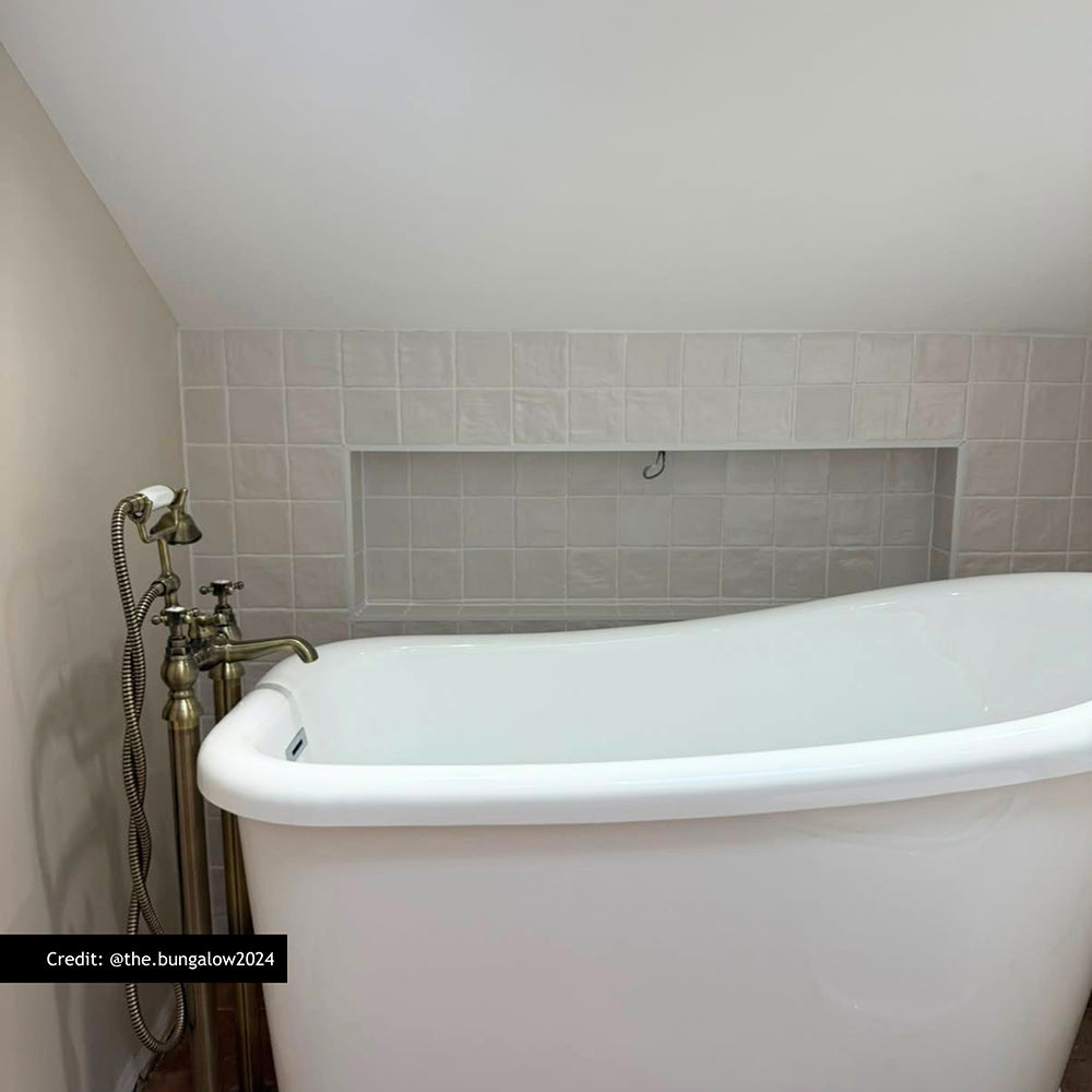 Customer bathroom featuring Zellige Oyster Square Moroccan style porcelain tiles in 10cm x 10cm. Gloss white handmade effect square tiles create a timeless bath surround and recessed shelf, pairing beautifully with a freestanding bath and traditional brass taps.